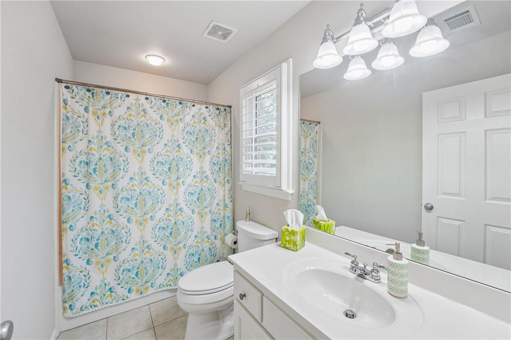 Bathroom with a white vanity, shuttered window, and blue-and-yellow patterned shower curtain.