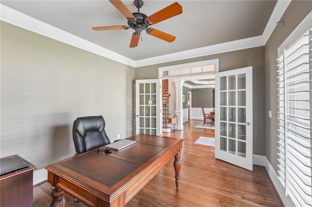 Furnished home office with a large wooden desk, French doors, hardwood floors, and a ceiling fan.