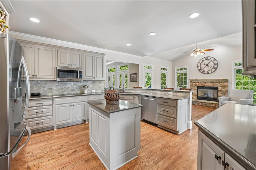 Open kitchen with a central island, white cabinets, hardwood floors, and an adjoining living area with a stone fireplace.