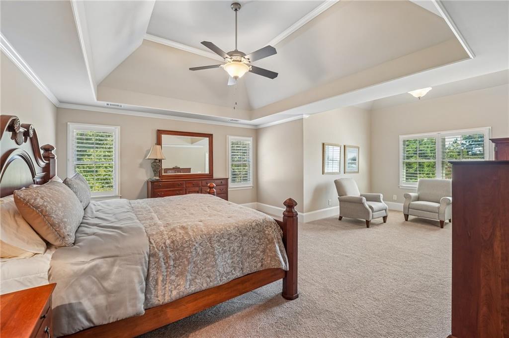 Spacious bedroom with a wooden bed, two armchairs, and a tray ceiling.