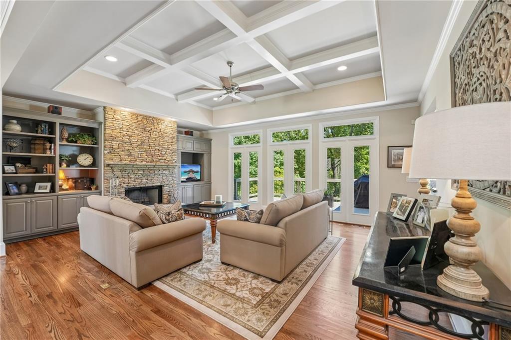 Living room with a coffered ceiling, stone fireplace, built-in cabinetry, and tall glass doors.