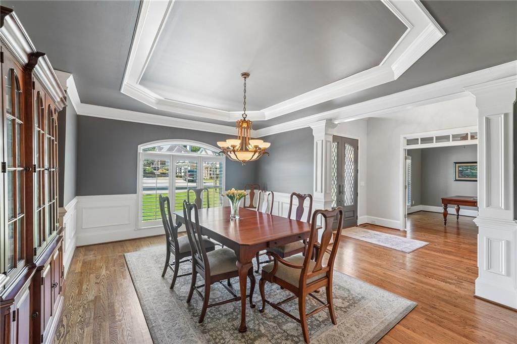 Dining room with a wooden table, arched window, tray ceiling, and dark wood cabinets.