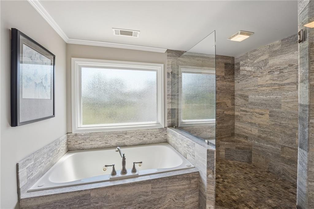 Bathroom with a built-in soaking tub beneath frosted windows and a glass-enclosed stone-tile shower.