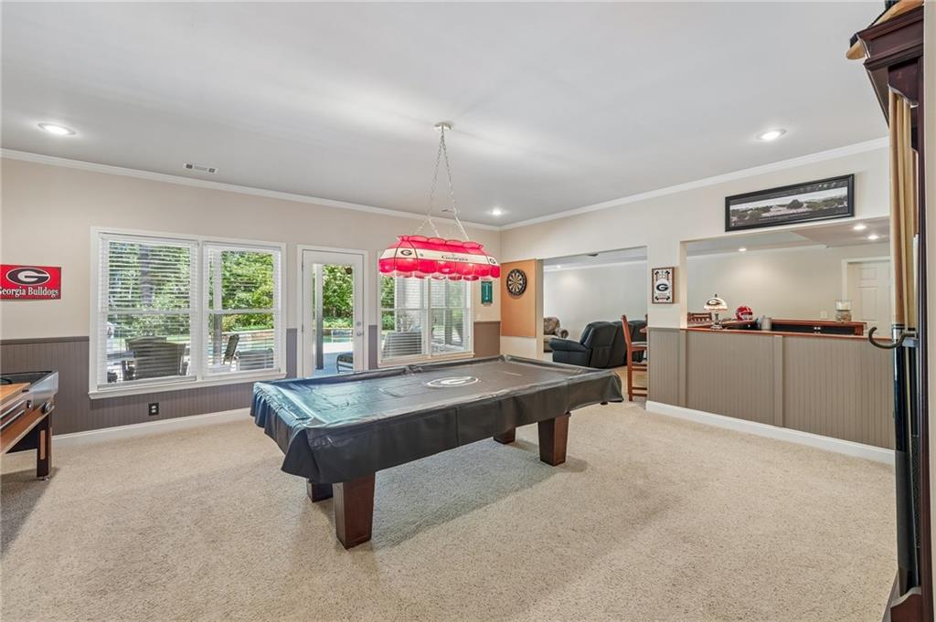 Game room with a pool table, red billiards light, and windows overlooking a patio.