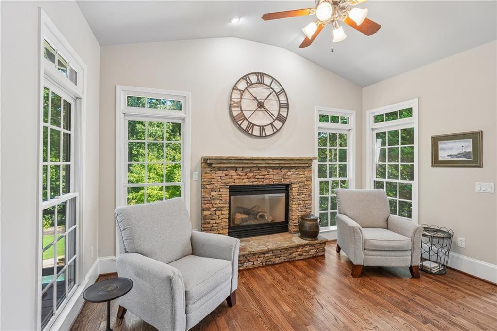 Living room with a stone fireplace, tall windows, hardwood floors, and two upholstered armchairs.