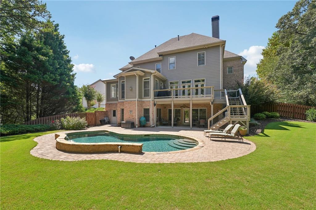 Rear of a two-story house with a raised deck overlooking a curved pool and brick patio.