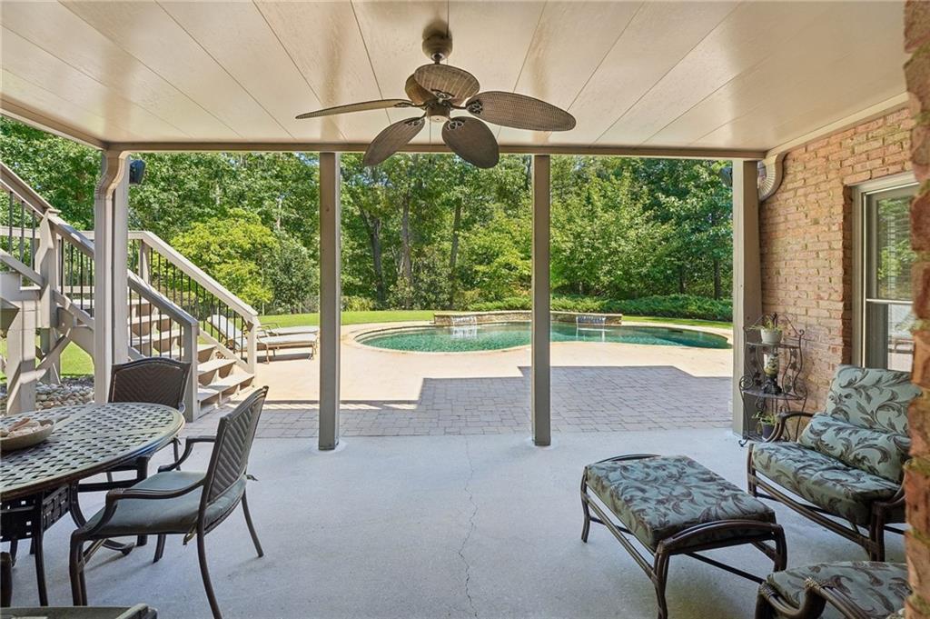Covered patio with dining and lounge seating overlooking a swimming pool and wooded yard.