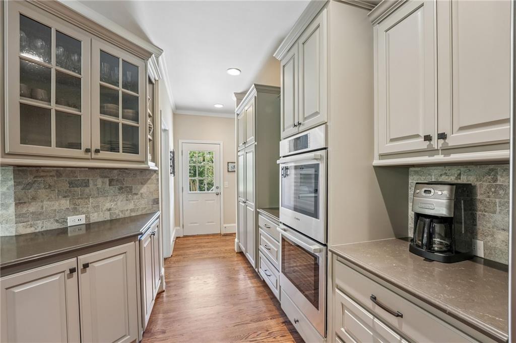 Galley kitchen with glass-front cabinets, stone backsplash, and built-in stainless steel appliances.