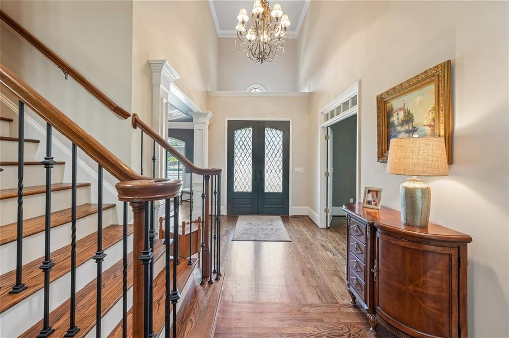 Entry foyer with a wood staircase, glass-paneled double doors, hardwood floors, and a chandelier.