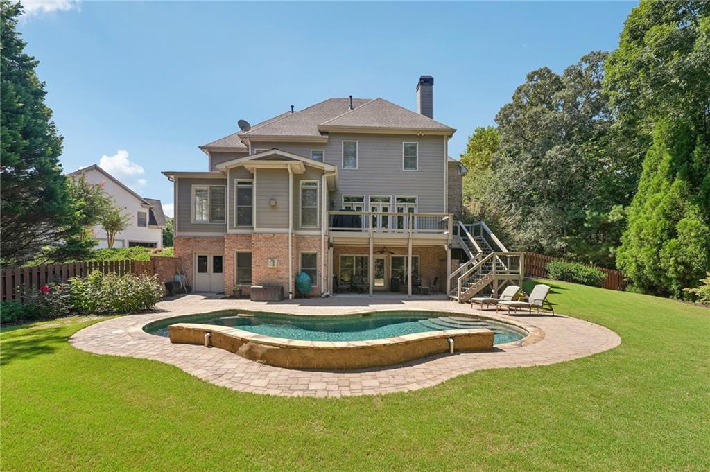 Two-story home overlooking a curved swimming pool and stone patio in a tree-lined backyard.