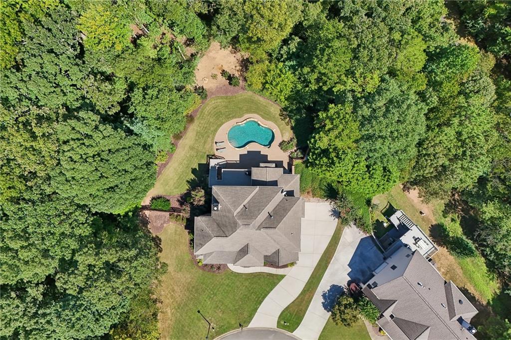 Aerial view of a house with a backyard pool, lawn, and surrounding trees.