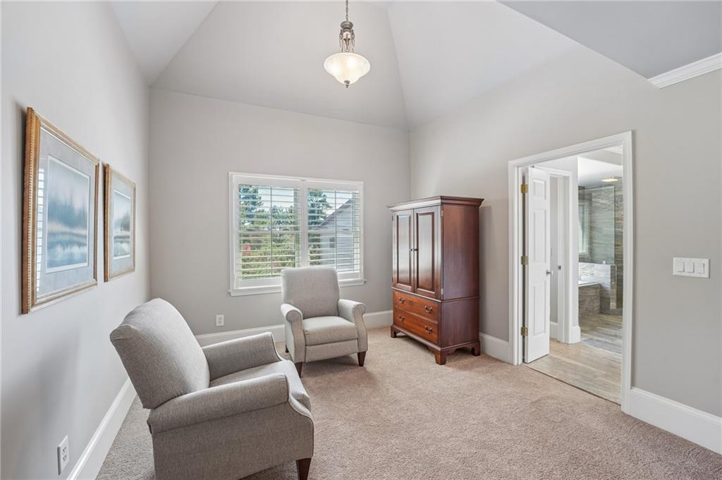 Sitting room with a vaulted ceiling, two armchairs, and a wooden armoire beside an open bathroom doorway.