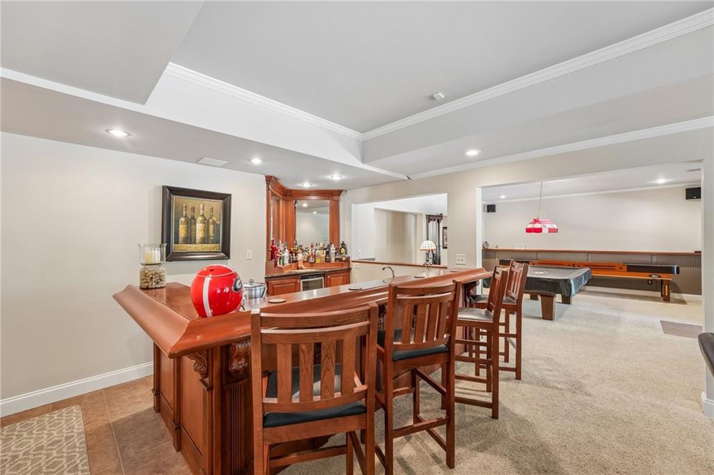 Basement game room with a wooden bar, bar stools, pool table, and long game table.