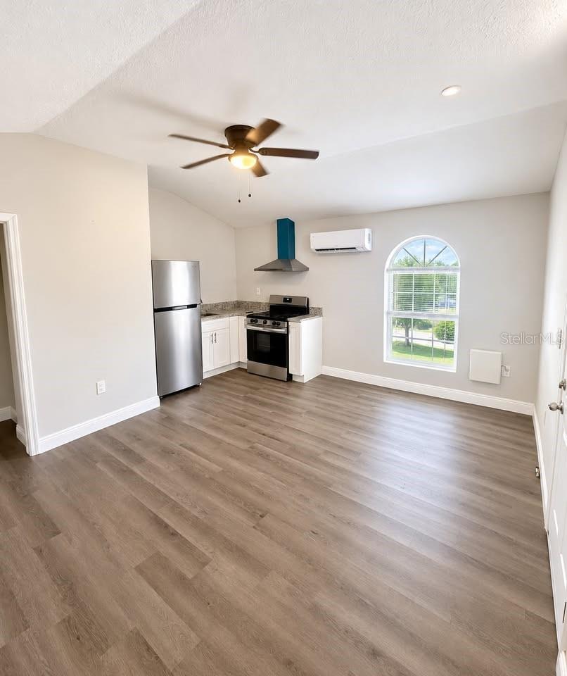 Vacant kitchen with stainless steel appliances, wood-look floors, and an arched window.