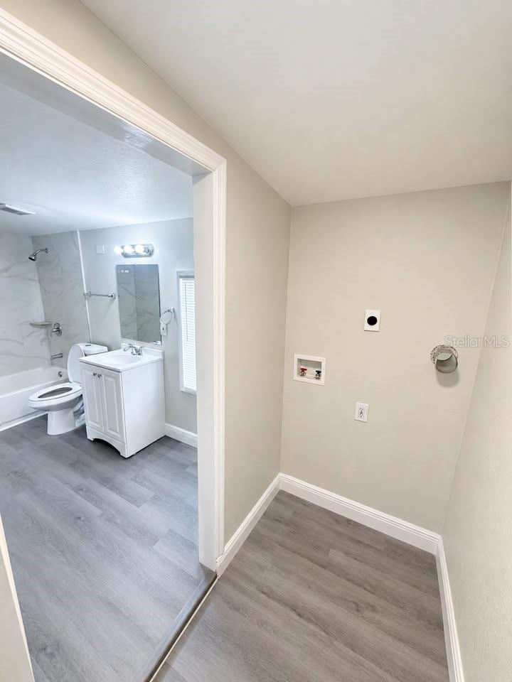 Empty laundry area with washer hookups beside a bathroom with a white vanity and tub-shower.