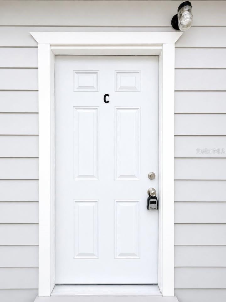 White exterior entry door marked C with a lockbox and horizontal siding.