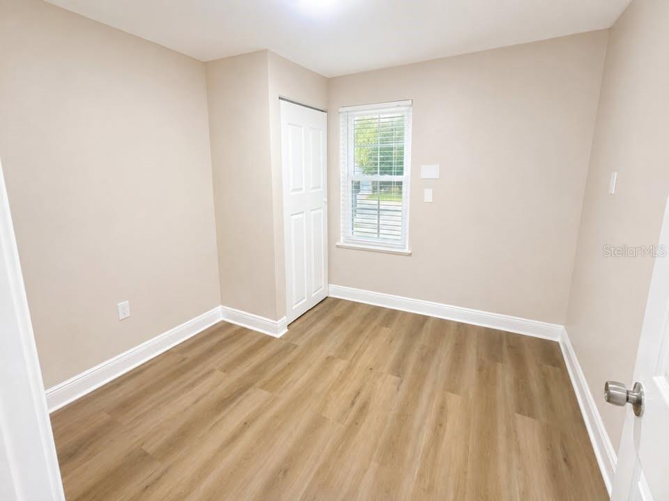 An empty room with wood-look flooring, beige walls, and a window beside a white door.