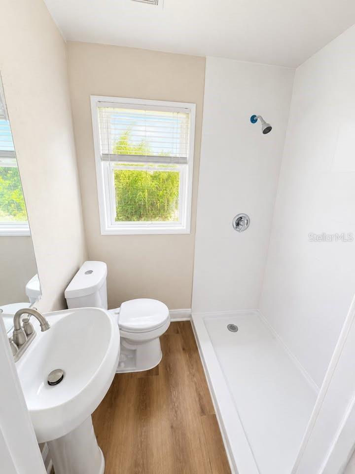 Bathroom with a white shower stall, pedestal sink, toilet, and window overlooking greenery.