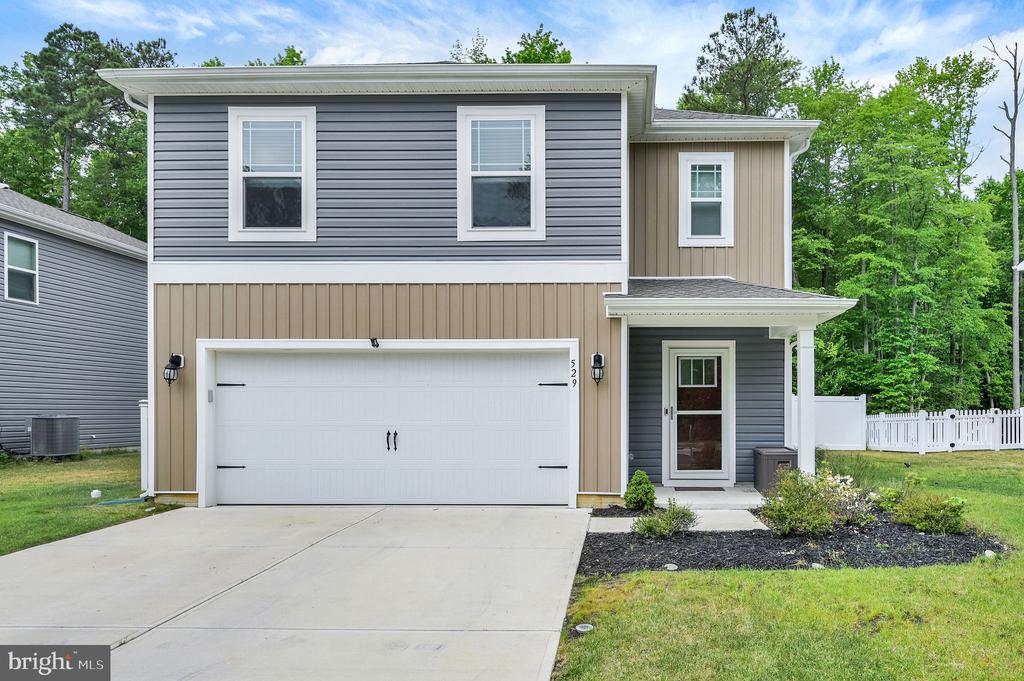 Two-story gray and tan home with a white double garage, driveway, and covered entry.