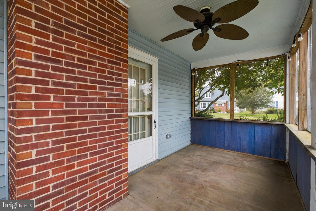 Covered porch with a ceiling fan, blue lower panels, and a red brick wall.