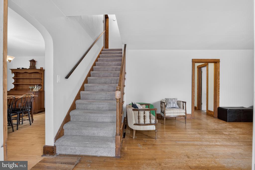 Foyer with carpeted staircase, hardwood floors, and a small sitting area.