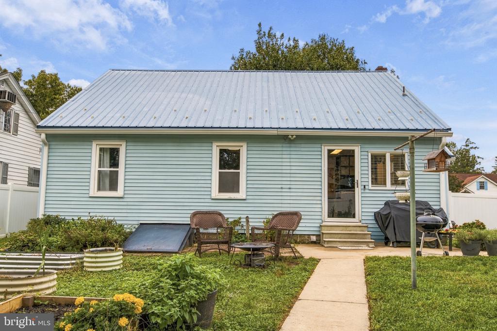 Rear of a light blue house with a metal roof, garden beds, and patio seating.