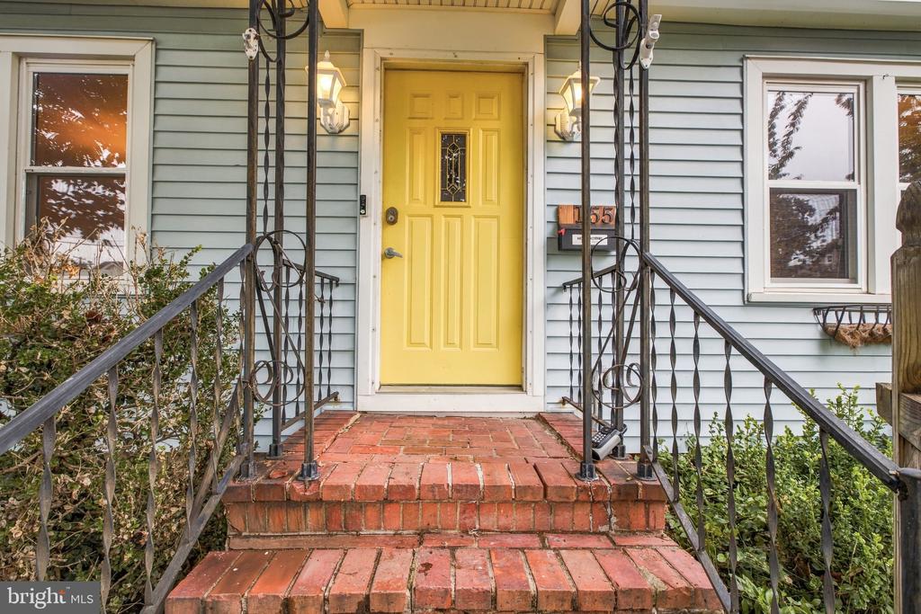 Home entrance with a yellow front door, brick steps, and black metal railings.