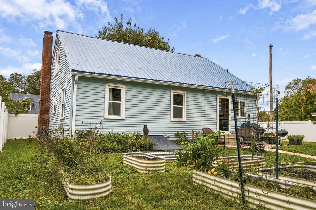 Light-blue house with a metal roof, brick chimney, patio, and raised garden beds.