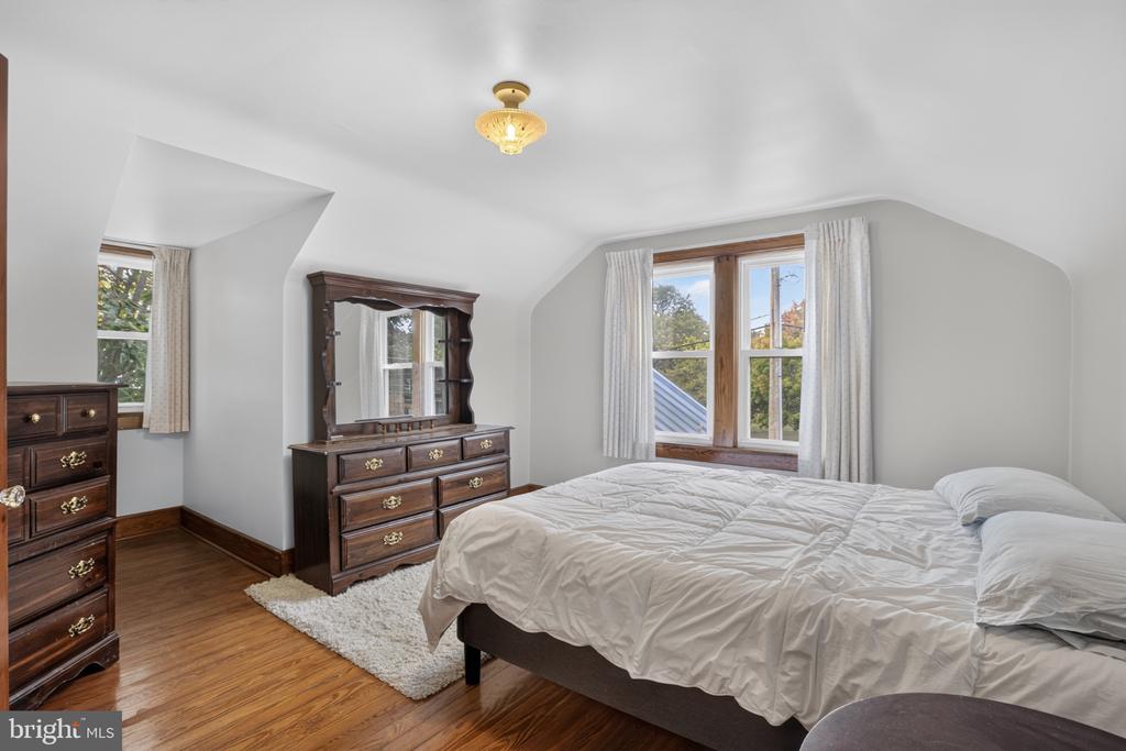 Furnished bedroom with a sloped ceiling, hardwood floors, and dark wood dressers beside two windows.
