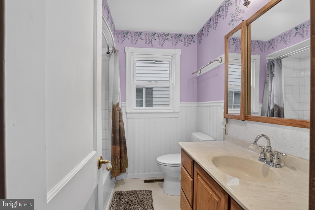 Bathroom with lavender walls, white wainscoting, shuttered window, and wood vanity.
