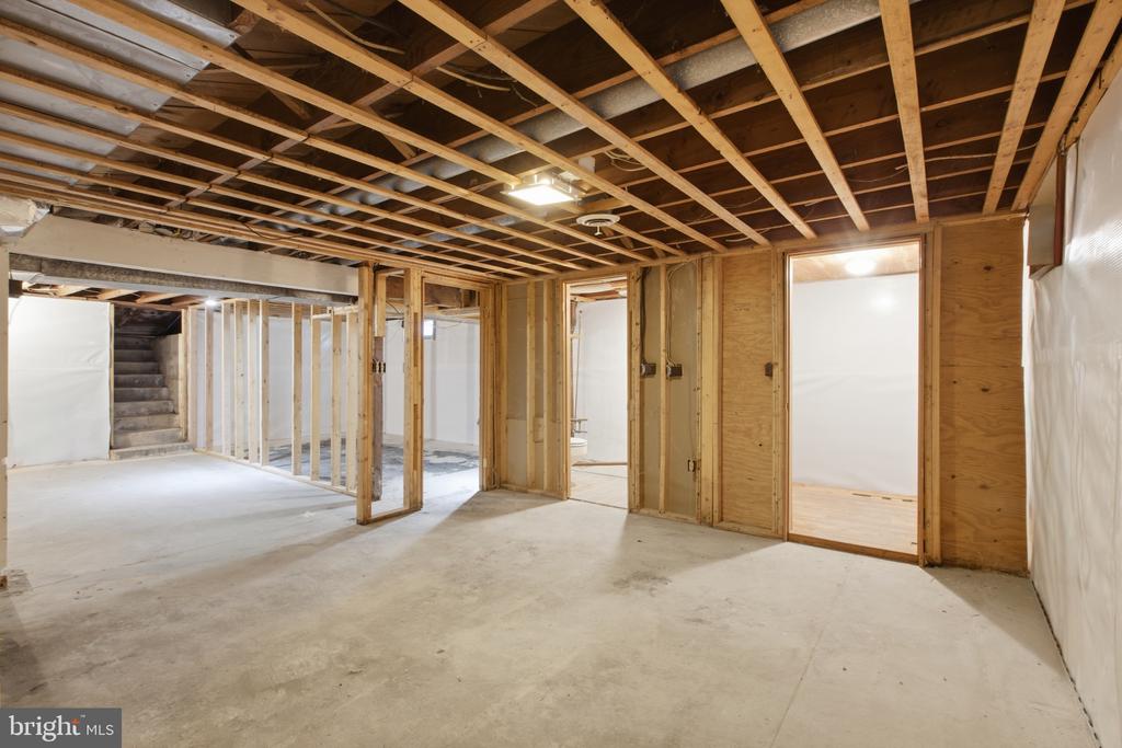 Unfinished basement with exposed ceiling framing, concrete floor, and a staircase at the back.