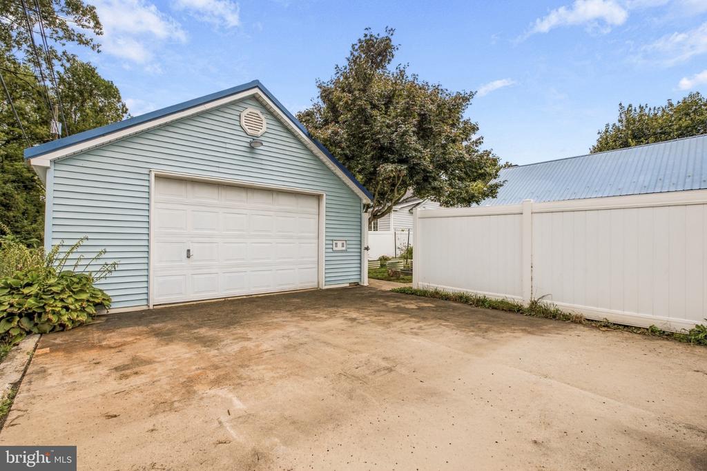 Light blue detached garage with a white door beside a broad concrete driveway and privacy fence.