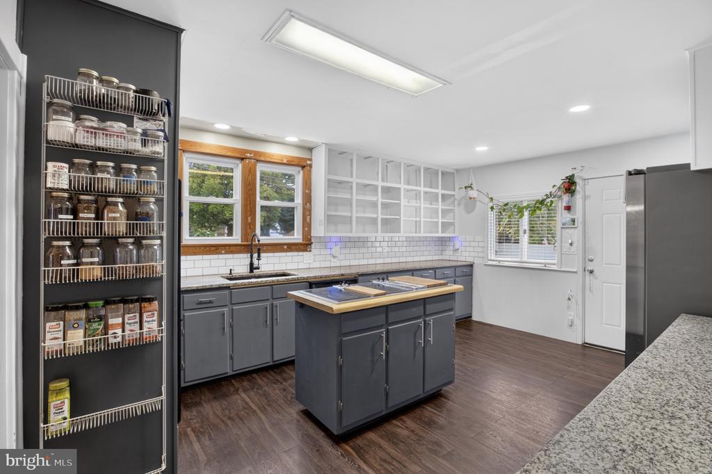 Kitchen with gray cabinets, a central island, open shelving, and wood-trimmed windows.