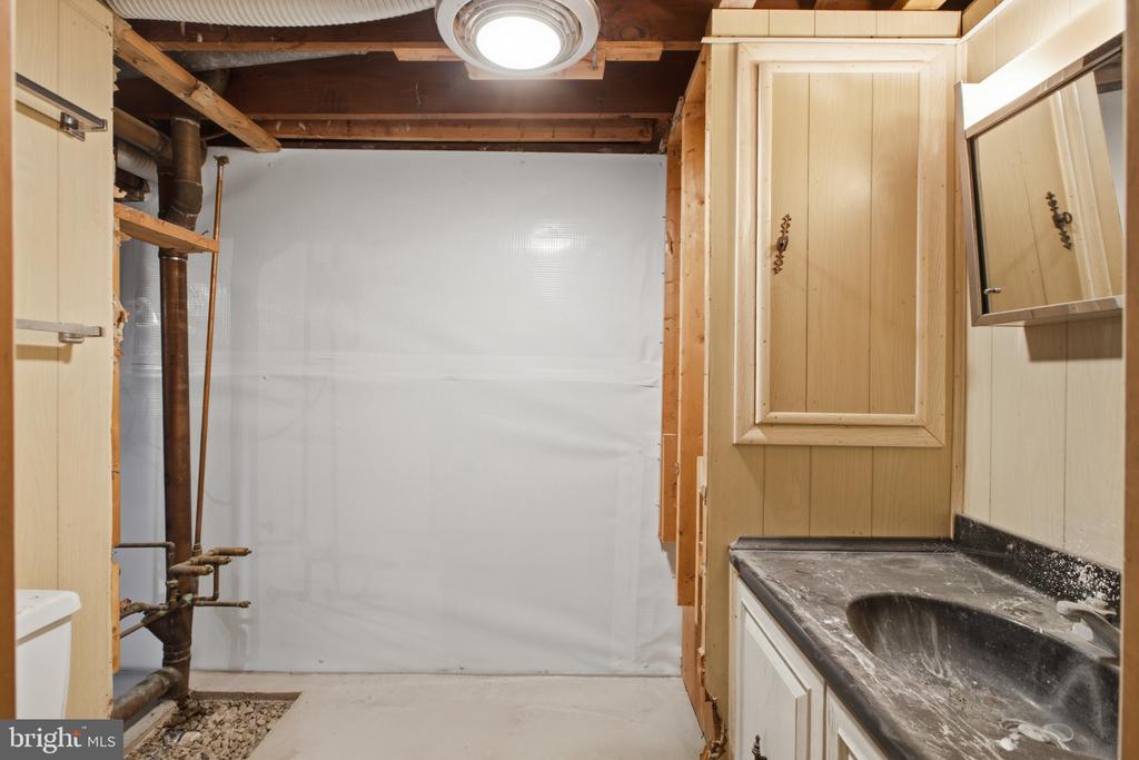 Basement utility area with a built-in sink, wood cabinets, exposed pipes, and an unfinished ceiling.