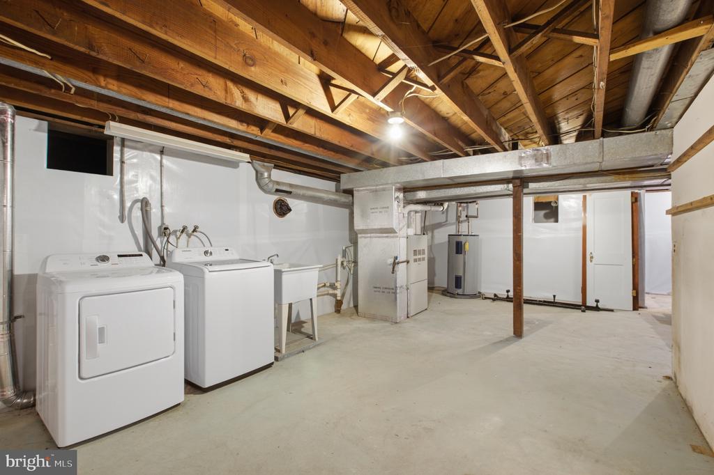Basement laundry area with washer and dryer beneath exposed wooden ceiling joists.