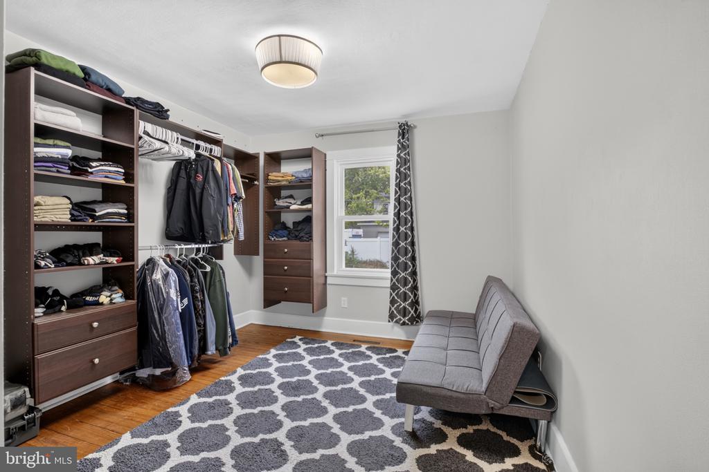 Walk-in closet with dark wood storage, hanging clothes, and a gray sofa.