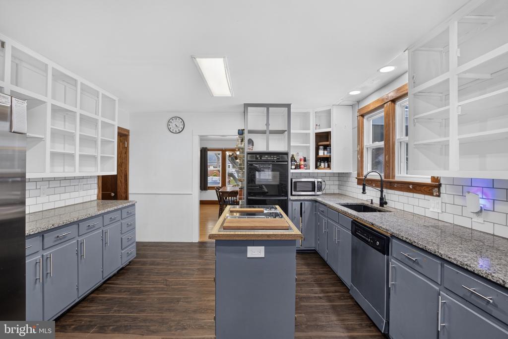 Kitchen with gray cabinetry, central island, open shelving, and long granite counters.