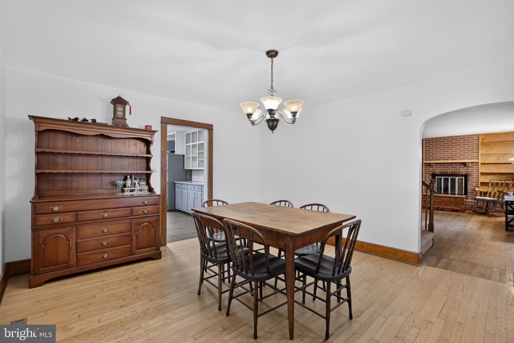 Dining room with a wooden table and hutch, hardwood floors, and an archway to a brick fireplace.