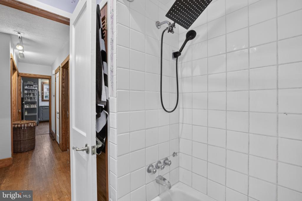 Bathroom with a white tiled tub-shower, rain showerhead, and handheld wand.