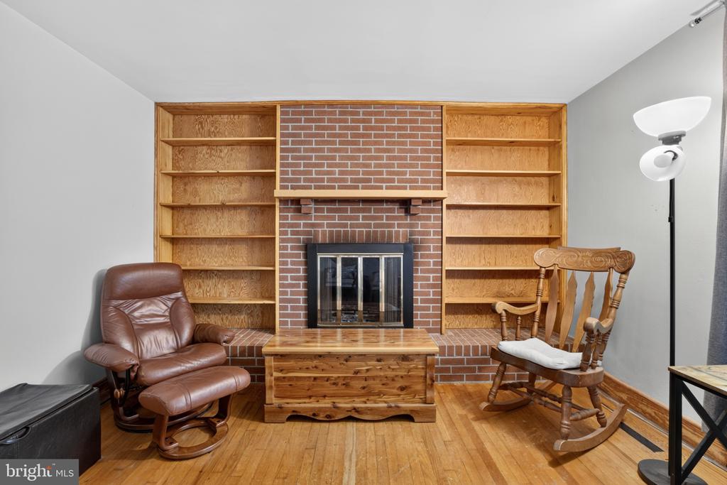 Living room with a brick fireplace, built-in wooden shelves, and leather and rocking chairs.