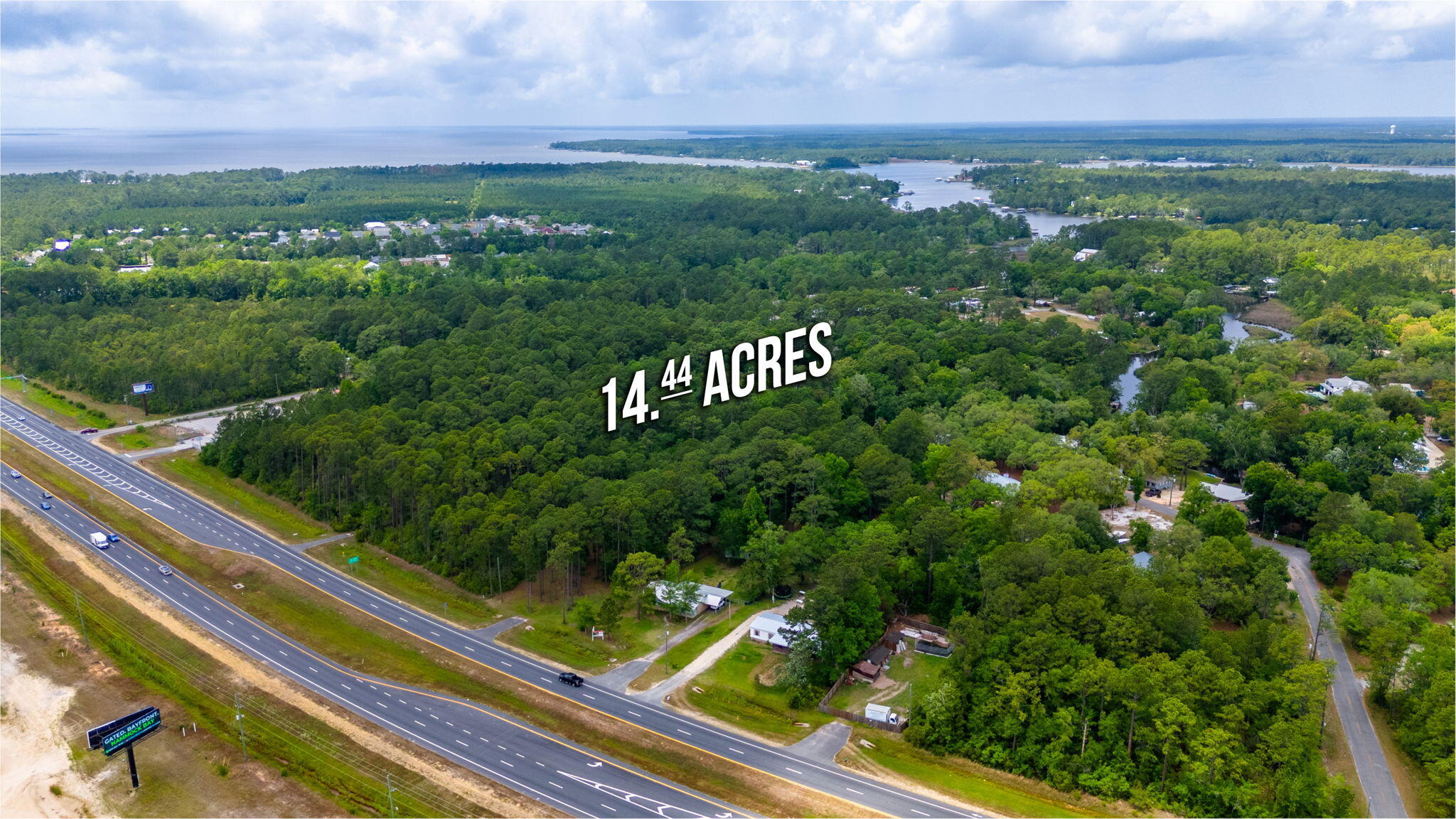 Aerial view of 14.44 wooded acres beside a divided highway, with waterways in the distance.