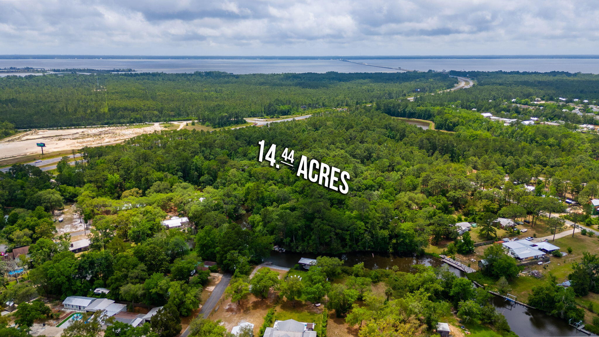 Aerial view of a wooded 14.44-acre property near water and a highway.