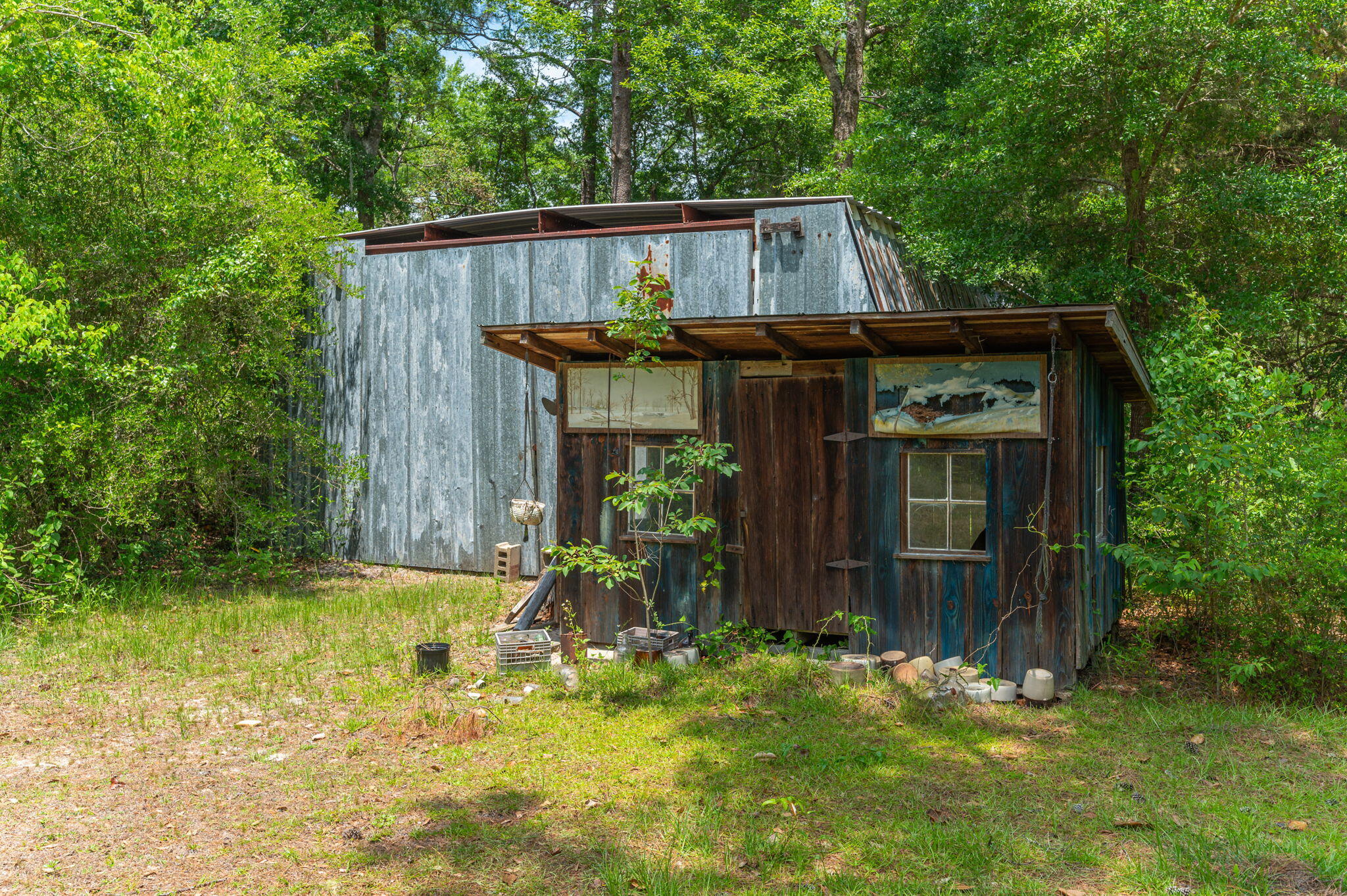 Weathered outbuilding with corrugated metal siding and wooden facade among trees.