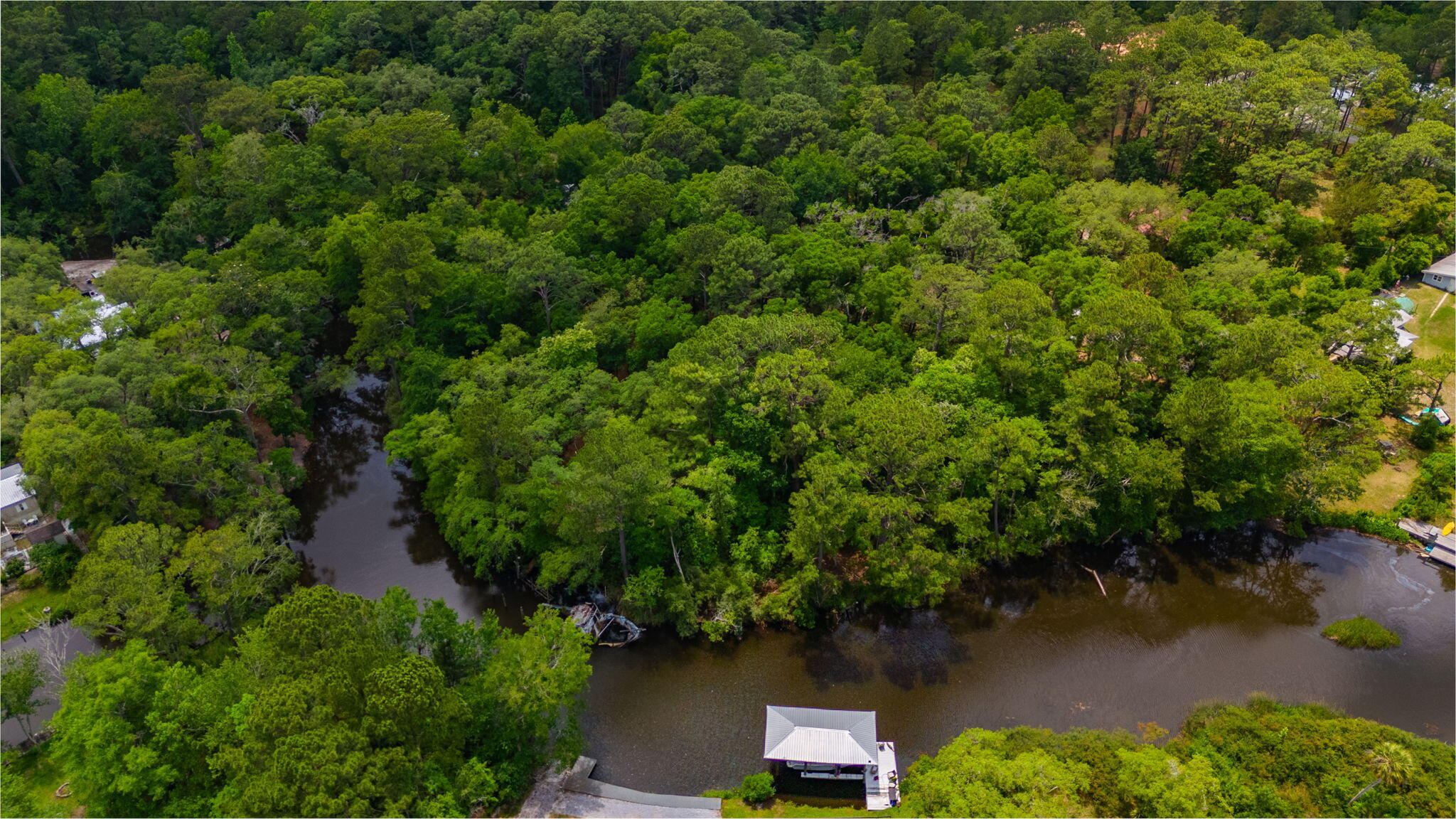Aerial view of a wooded waterfront property with a winding creek and covered dock.