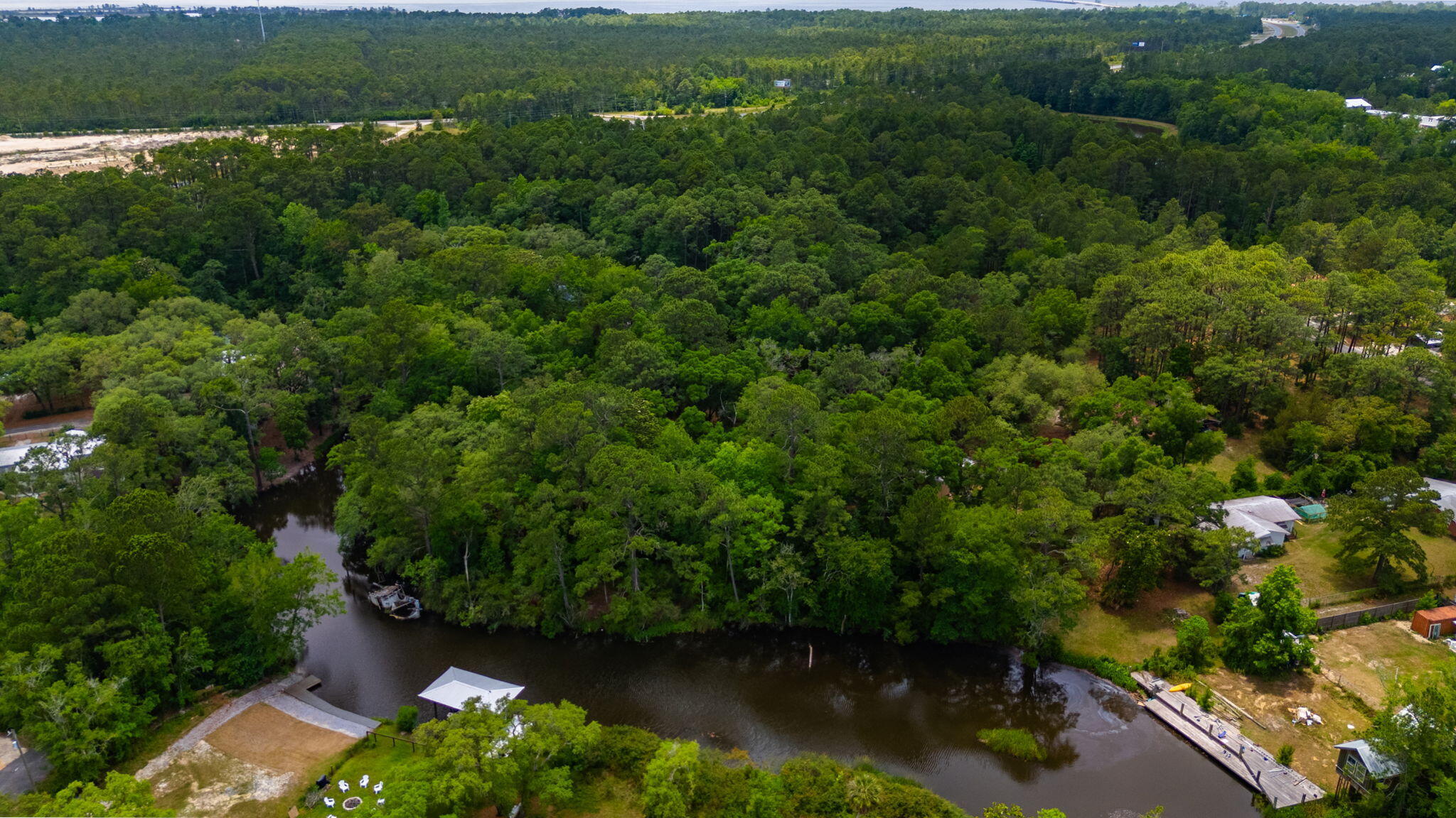 Aerial view of wooded land along a winding river, with docks and a highway in the distance.