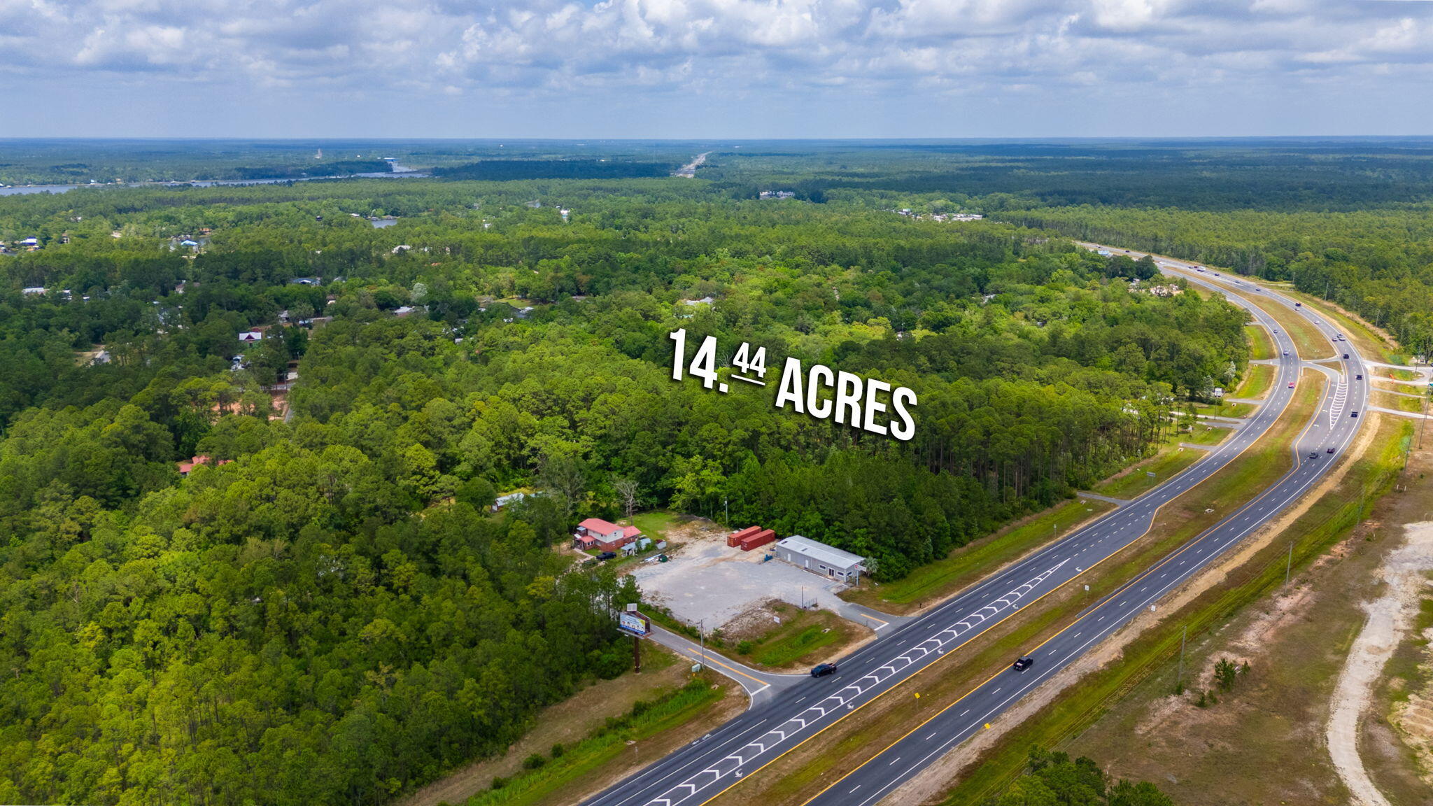 Wooded 14.44-acre property beside a divided highway, with a cleared area and buildings near the road.