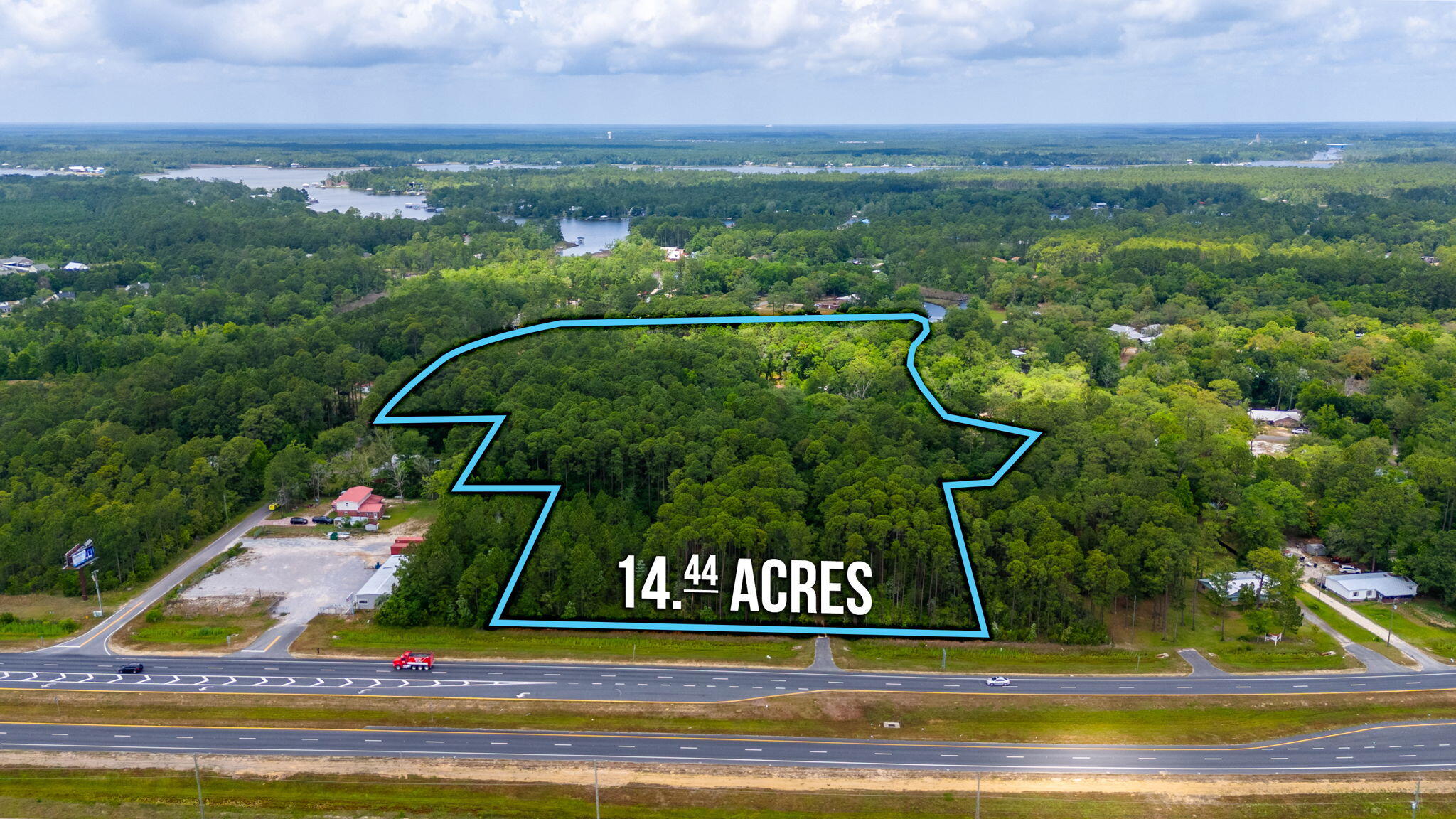 Aerial view of a wooded 14.44-acre parcel outlined in blue beside a divided highway.