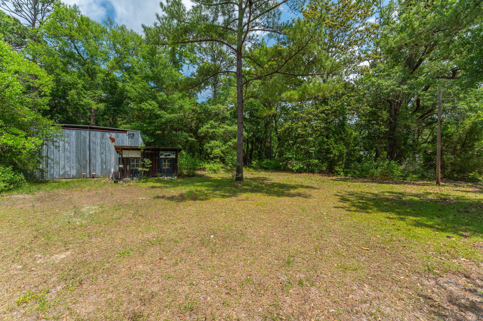 Weathered metal-sided building beside a grassy clearing surrounded by trees.