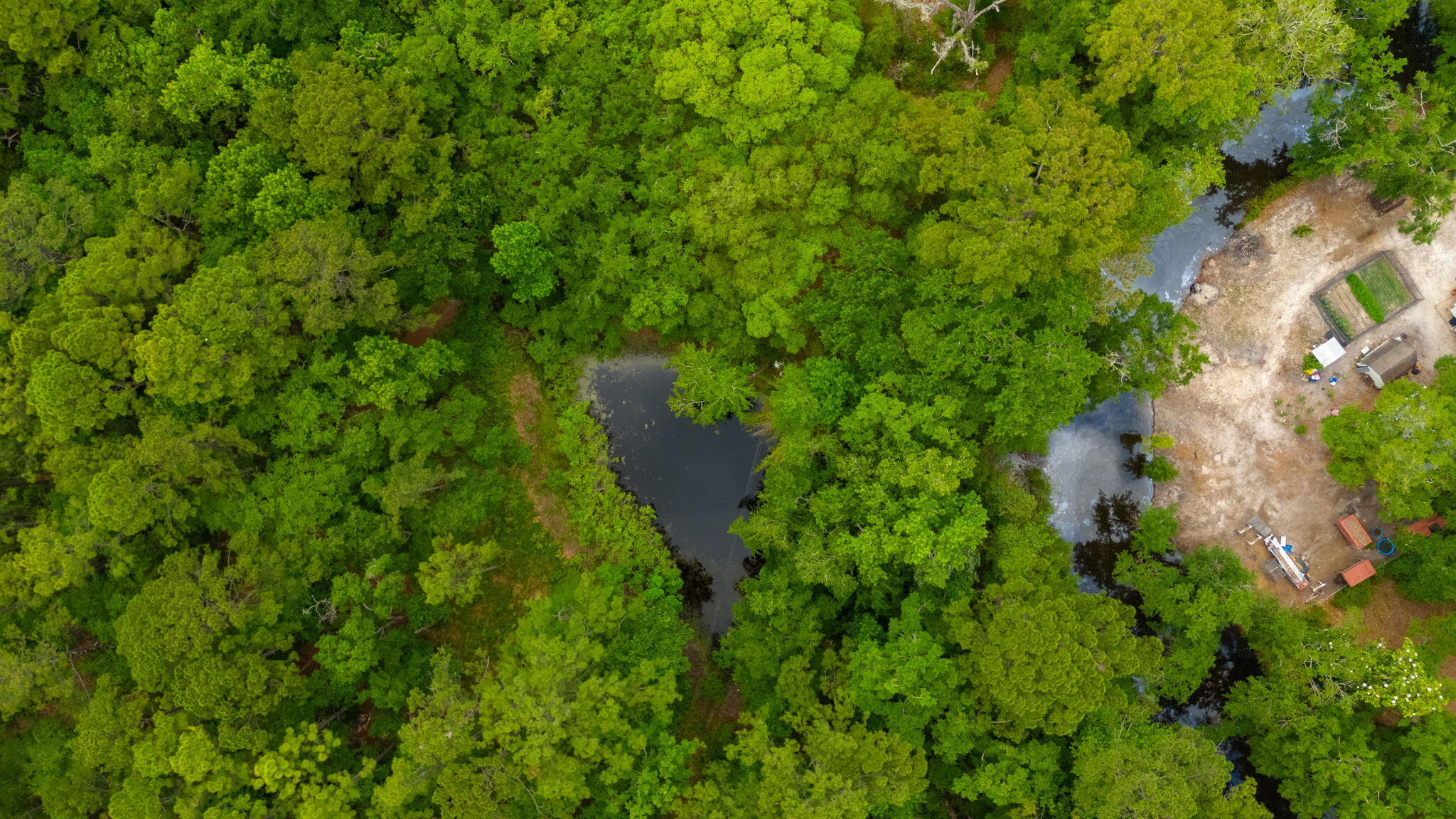 Aerial view of wooded land with ponds and a cleared area containing small structures.