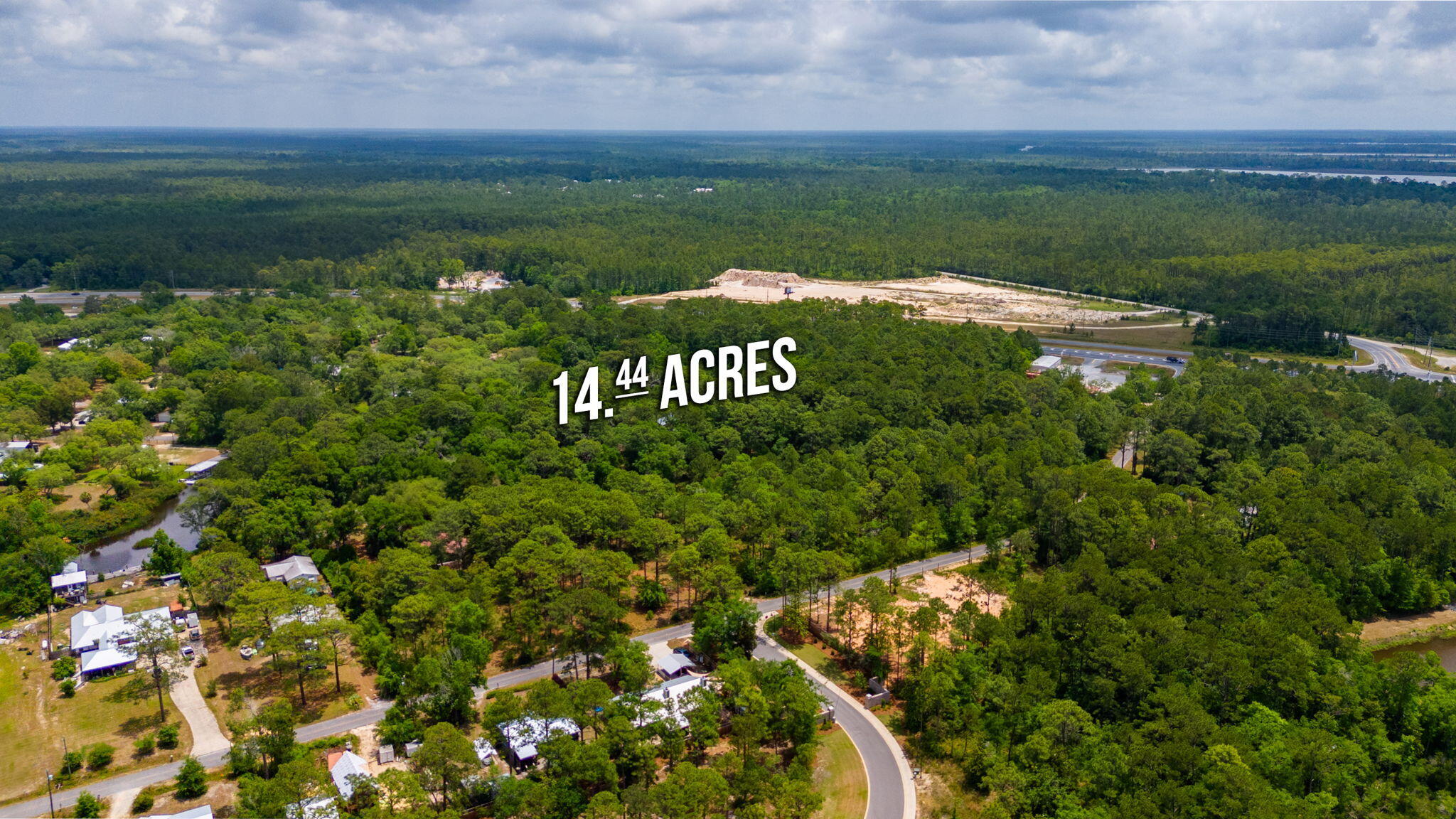 Aerial view of wooded 14.44-acre property with nearby roads, homes, and a cleared area.